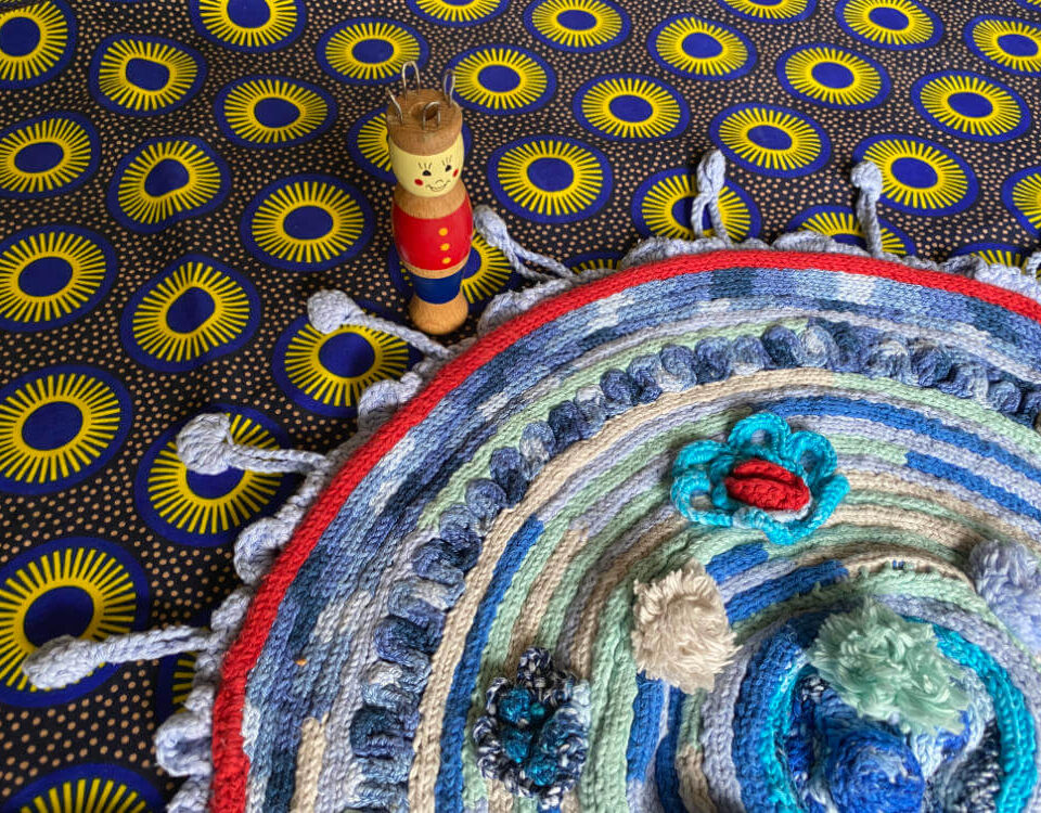 knitting doll stands besides circular rug made of knitting-doll-cords