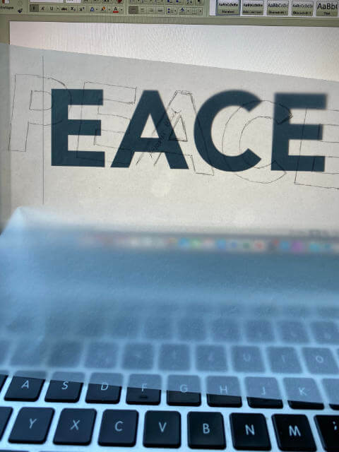 tracing the word PEACE on the laptop on translucent paper
