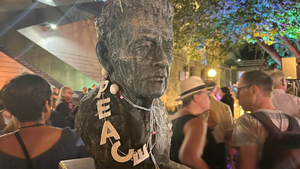 monument of a man with peace-necklace surrounded by people