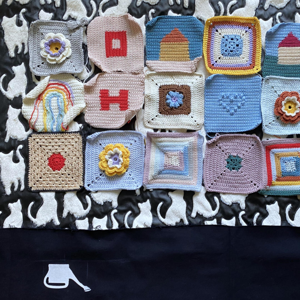 many unique colorful granny squares on a black and white piece of cloth with cats