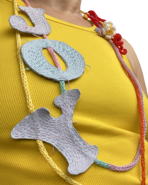 textile necklace with JOY-letters and crocheted flowers on yellow top