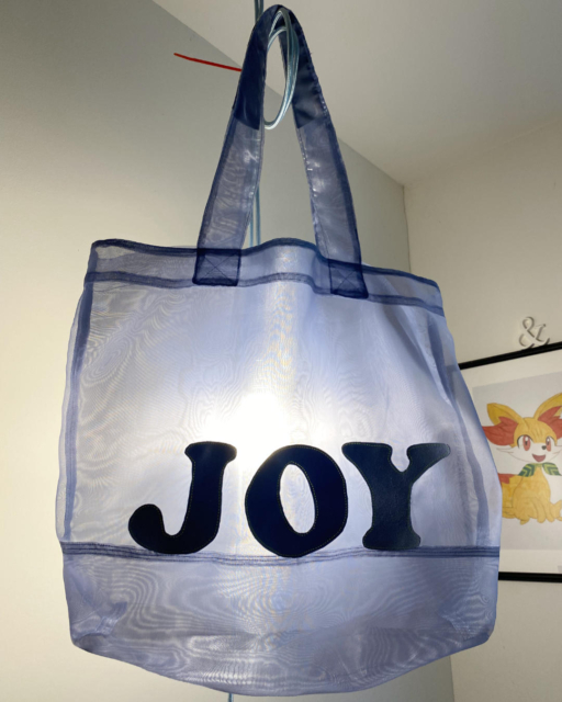 finished totebag JOY hanging on lampstring with light behind