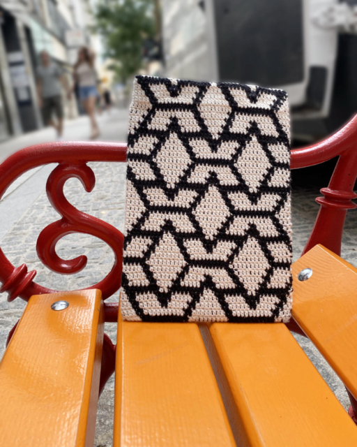 black-white iPad sleeve in tapestry crochet leaning on an orange bench with red railing