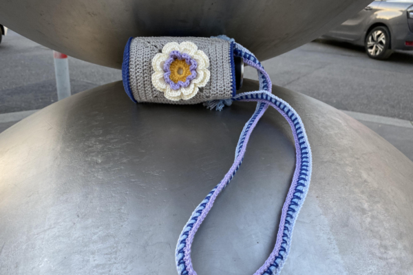 small crocheted bottle bag with flowers lying between two huge metal spheres