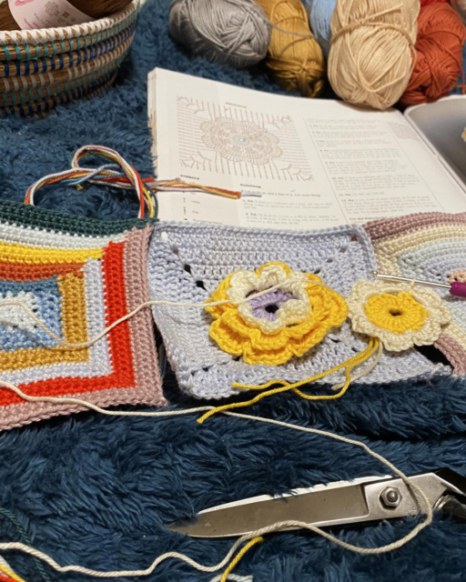 3 granny squares in the making with a crochet hook on the pattern in a book