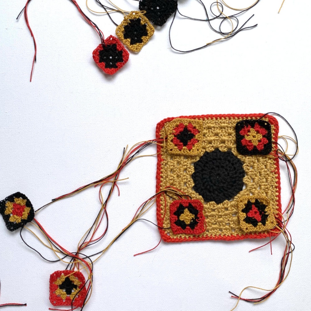 4 mini granny squares in red black ochre lying on big granny square