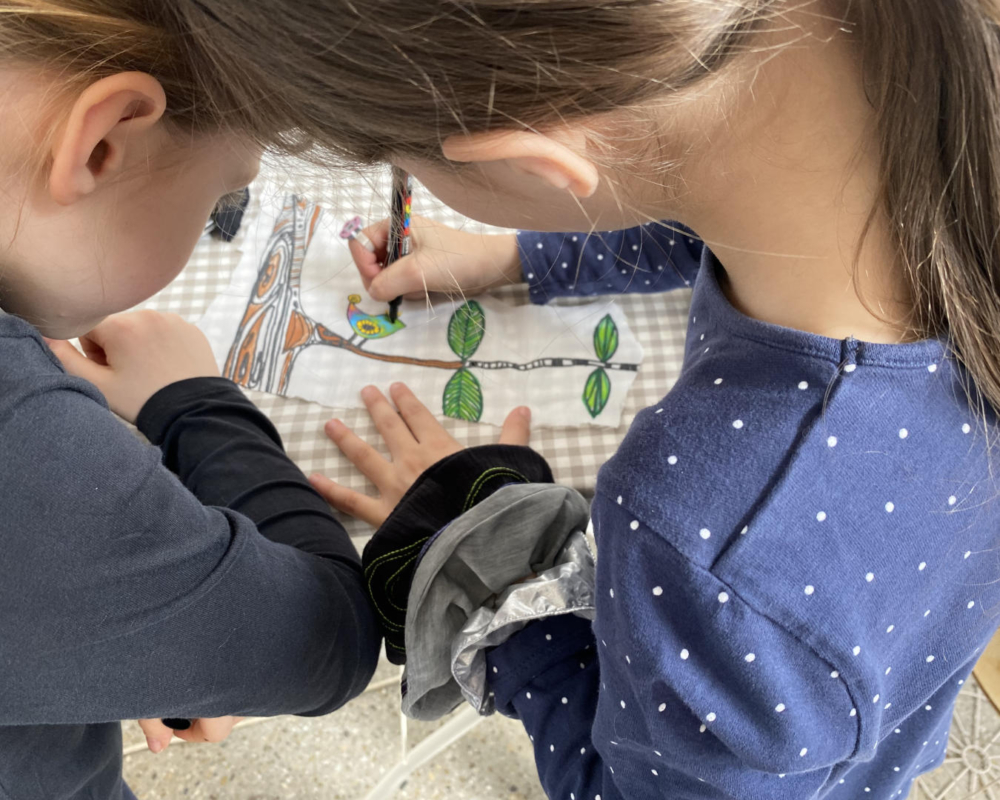 2 girls painting a bird on white cloth