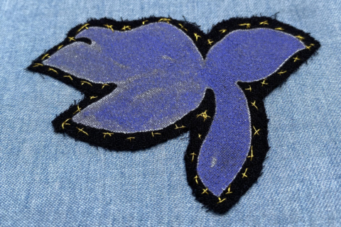 cut out lilac flower stitched on light blue cloth with golden thread