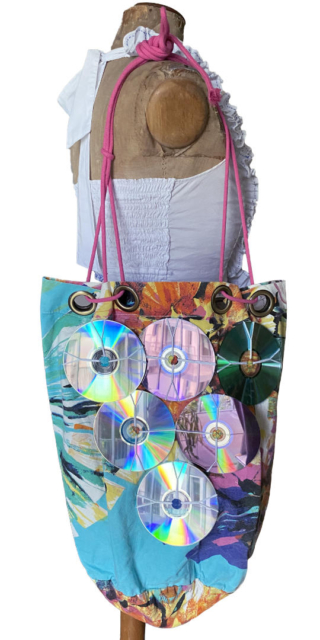 6 CDs attached in triangle pattern on colourful tote bag on mannequin